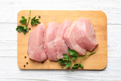 Photo of Board with cut raw turkey fillet and parsley on white wooden background, top view