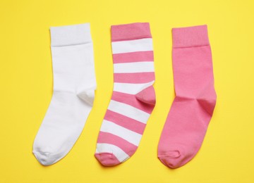 Photo of Different pink and white socks on yellow background, flat lay