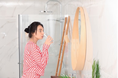 Young woman drinking water near mirror in bathroom