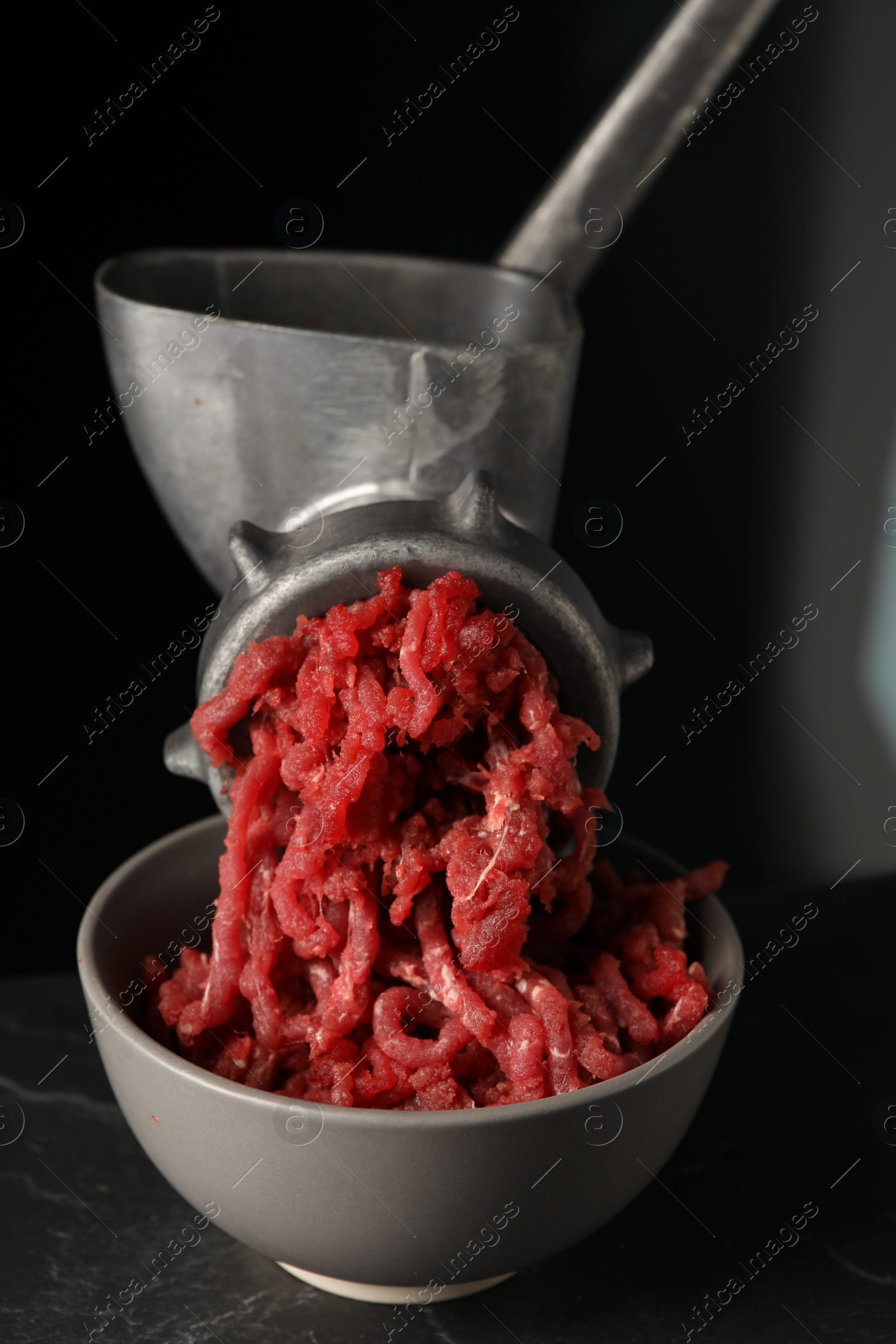 Photo of Metal meat grinder with beef mince on dark textured table against black background, closeup