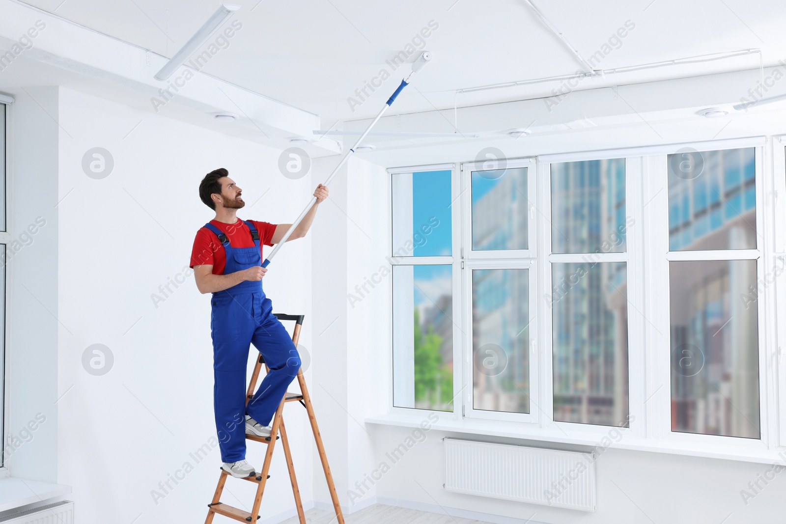 Photo of Handyman painting ceiling with roller on step ladder in room