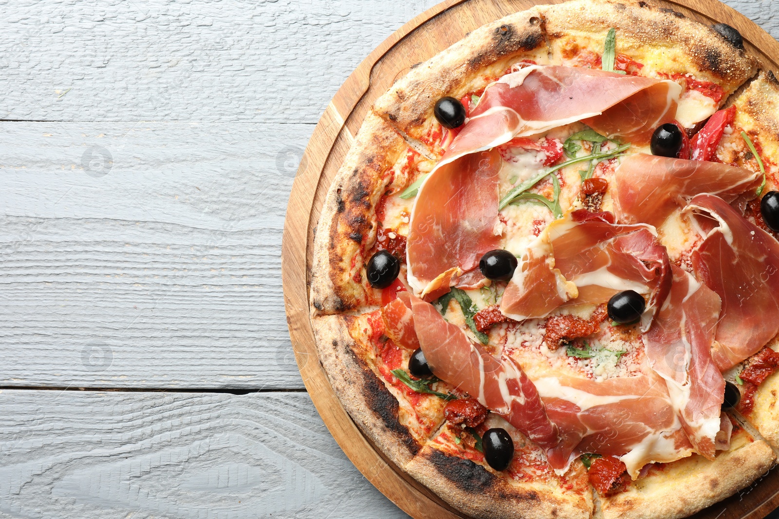 Photo of Tasty pizza with cured ham, olives and sun-dried tomato on gray wooden table, top view. Space for text