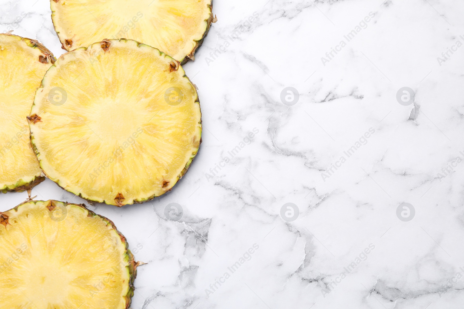 Photo of Slices of tasty ripe pineapple on white marble table, flat lay. Space for text