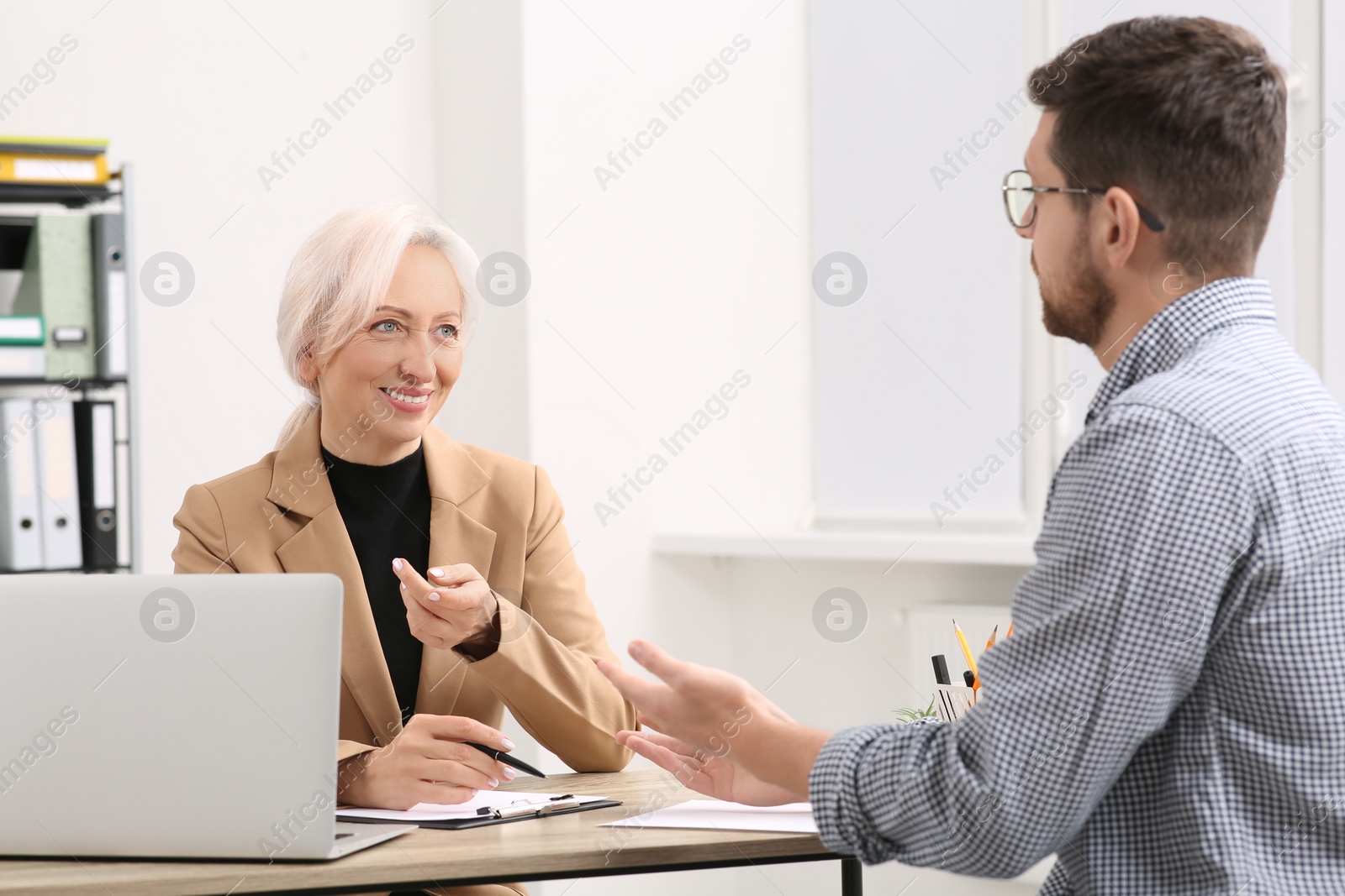 Photo of Happy woman having conversation with man at wooden table in office. Manager conducting job interview with applicant