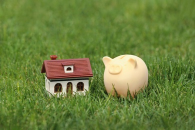 Photo of Piggy bank and model of house on green grass outdoors