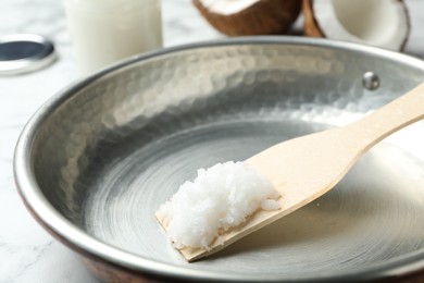 Photo of Frying pan with coconut oil and wooden spatula on white marble table, closeup. Healthy cooking
