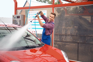 Male worker cleaning vehicle with high pressure water jet at car wash