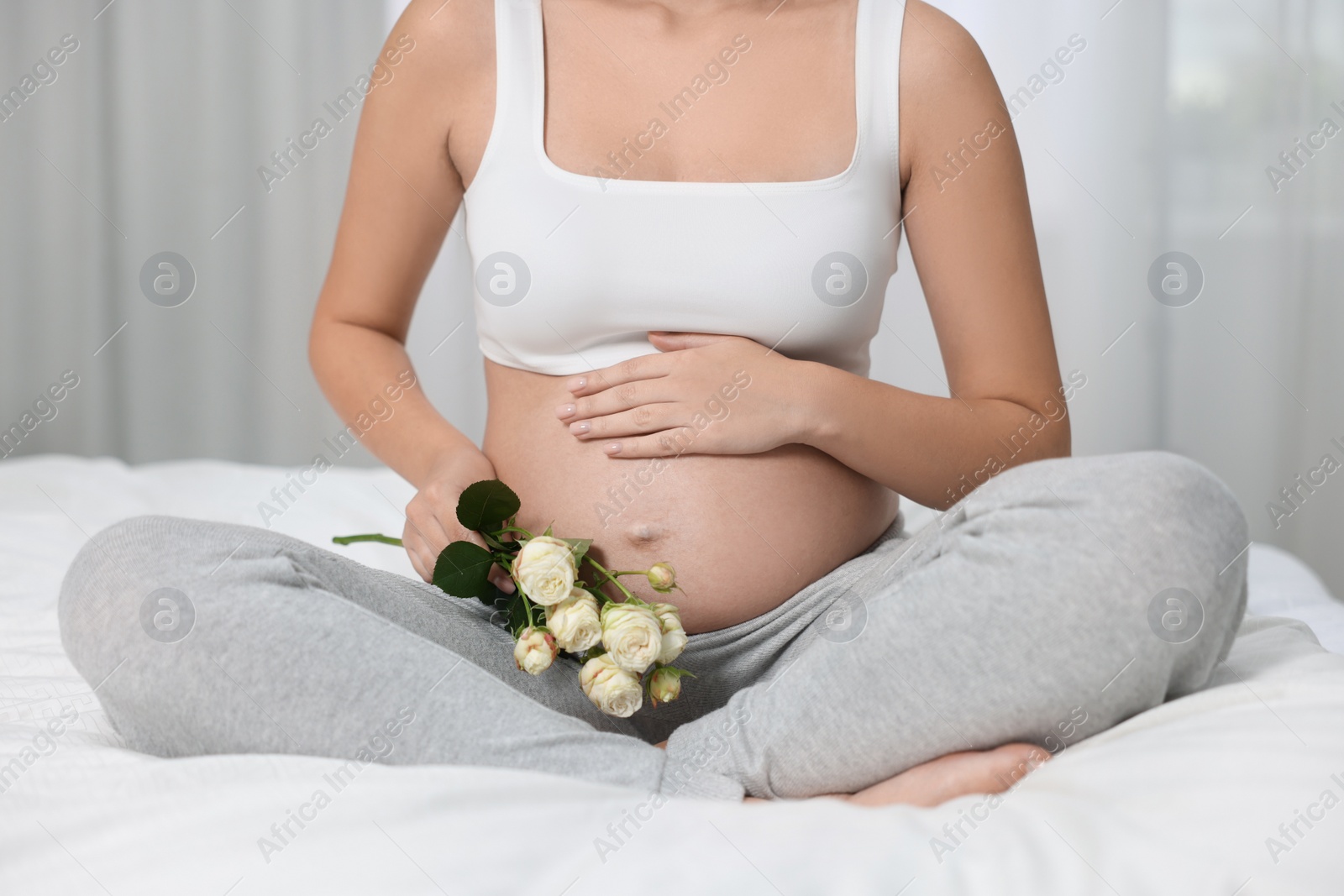 Photo of Pregnant woman with roses sitting on bed indoors, closeup