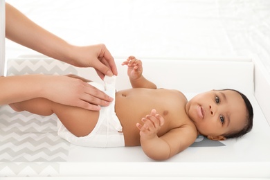 Photo of Mother changing her baby's diaper on table indoors