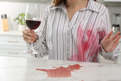 Photo of Woman with spilled wine over her shirt and marble table in kitchen, closeup