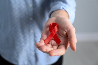 Photo of Woman holding red awareness ribbon indoors, closeup. World AIDS disease day