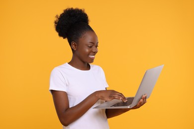 Photo of Happy young woman using laptop on orange background