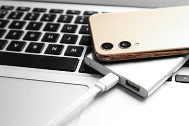Photo of Modern smartphone charging with power bank on laptop, closeup