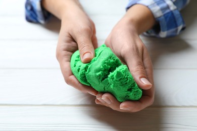 Photo of Woman playing with green kinetic sand at white wooden table, closeup