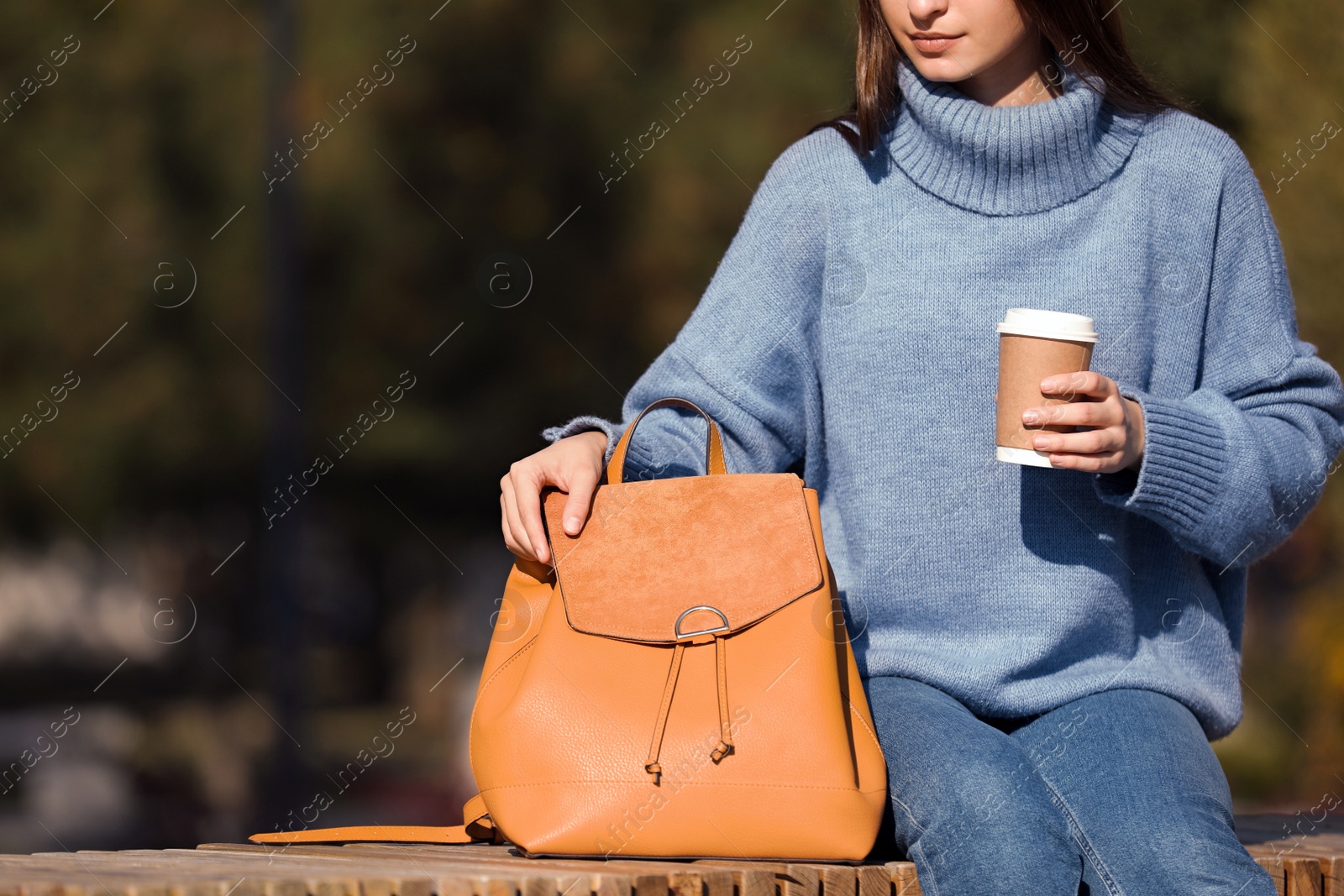 Photo of Young woman with stylish backpack and hot drink on autumn day, closeup. Space for text