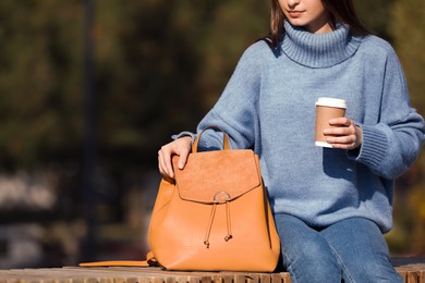 Photo of Young woman with stylish backpack and hot drink on autumn day, closeup. Space for text