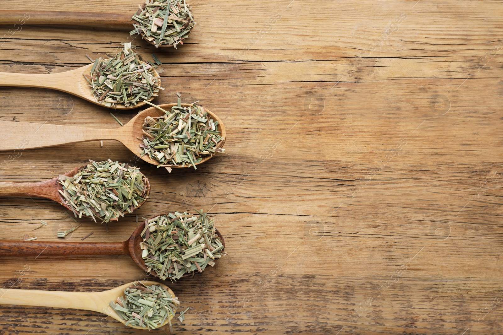 Photo of Many spoons with aromatic dried lemongrass on wooden table, flat lay. Space for text