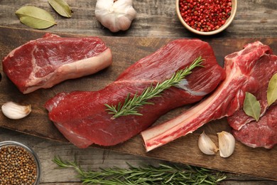 Photo of Pieces of raw beef meat and spices on wooden table, flat lay