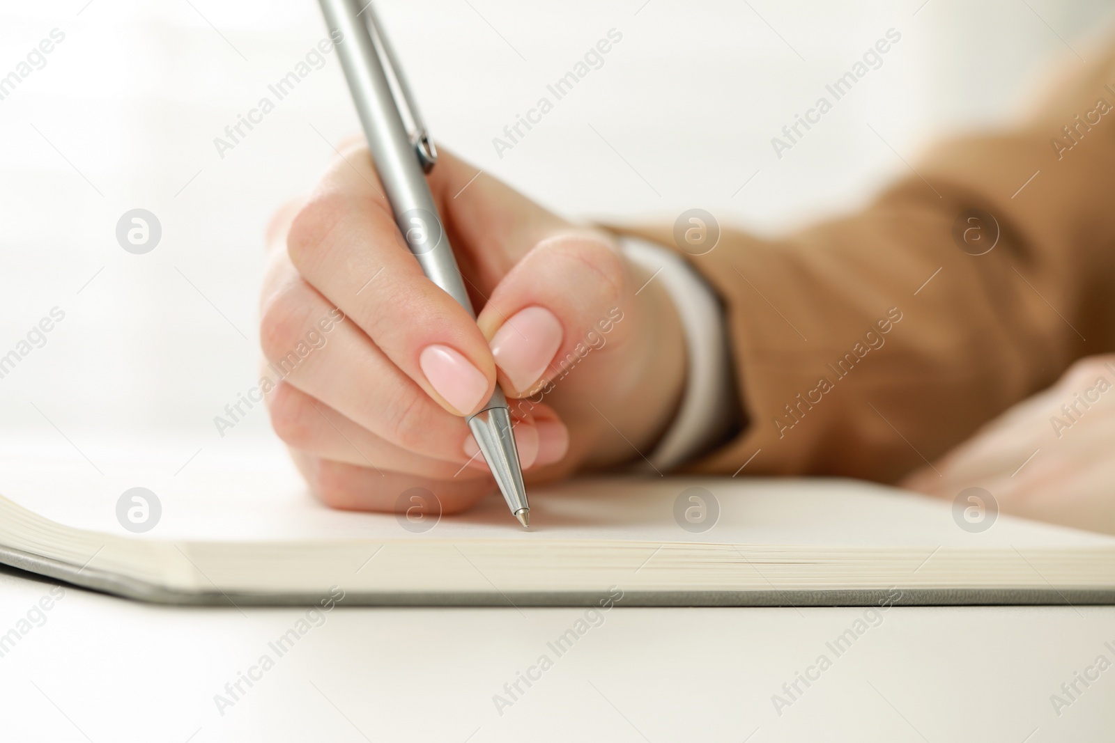 Photo of Woman writing in notebook at white table, closeup