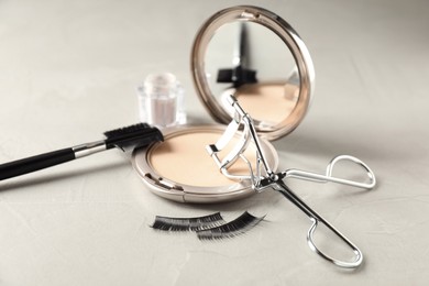 Eyelash curler and makeup products on grey table, closeup
