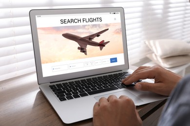 Man using laptop to book flight at wooden table, closeup