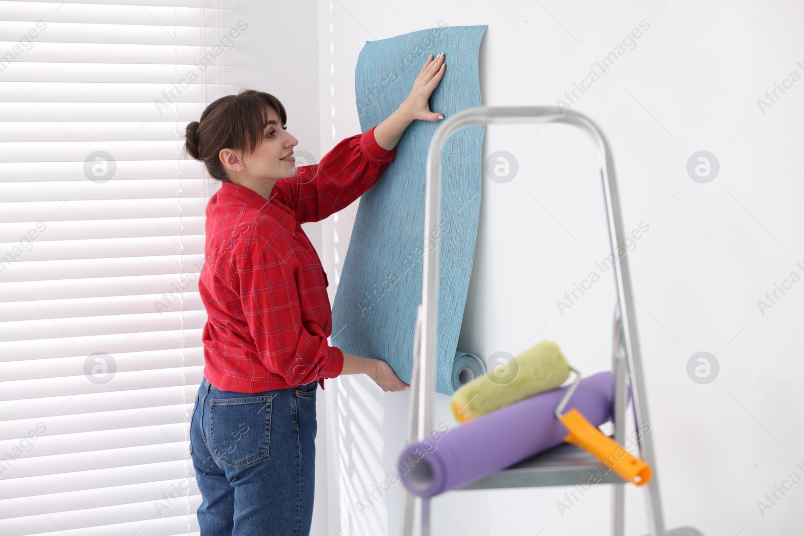 Photo of Woman hanging light blue wallpaper in room