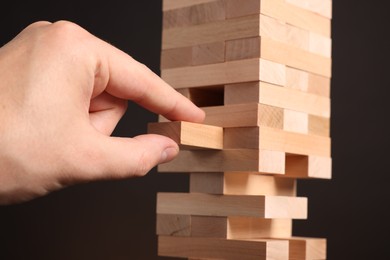 Photo of Playing Jenga. Man removing wooden block from tower on dark background, closeup