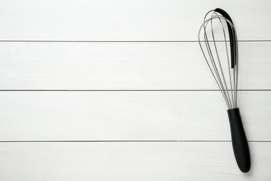 Metal whisk on white wooden table, top view. Space for text