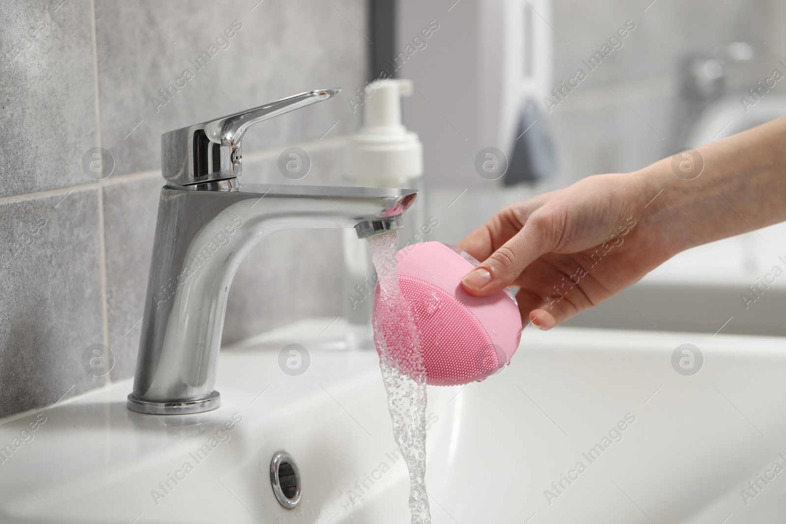 Photo of Young woman washing facial brush in bathroom, closeup