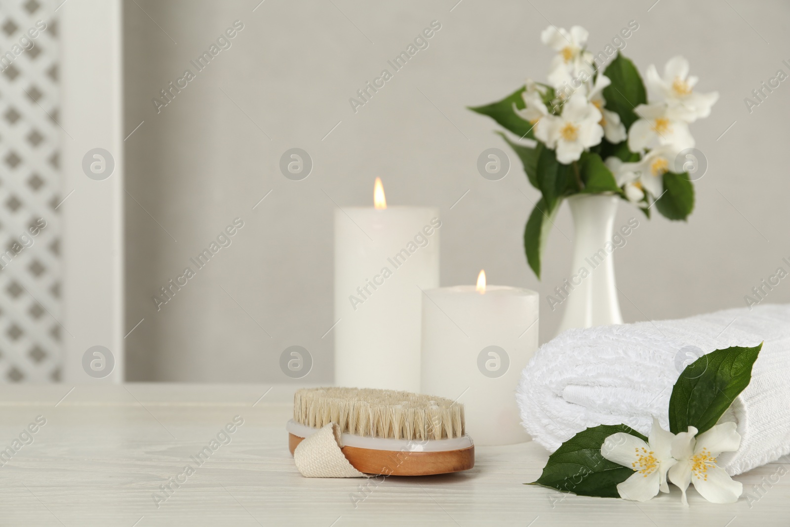 Photo of Beautiful jasmine flowers, brush and towel on white wooden table, space for text