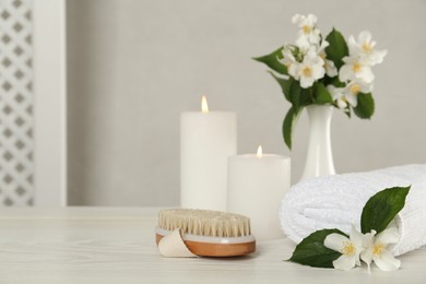 Beautiful jasmine flowers, brush and towel on white wooden table, space for text