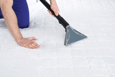 Man disinfecting mattress with vacuum cleaner, closeup. Space for text