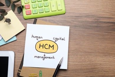 Photo of Paper with HCM abbreviation and space for text on wooden office table, flat lay. Human Capital Management