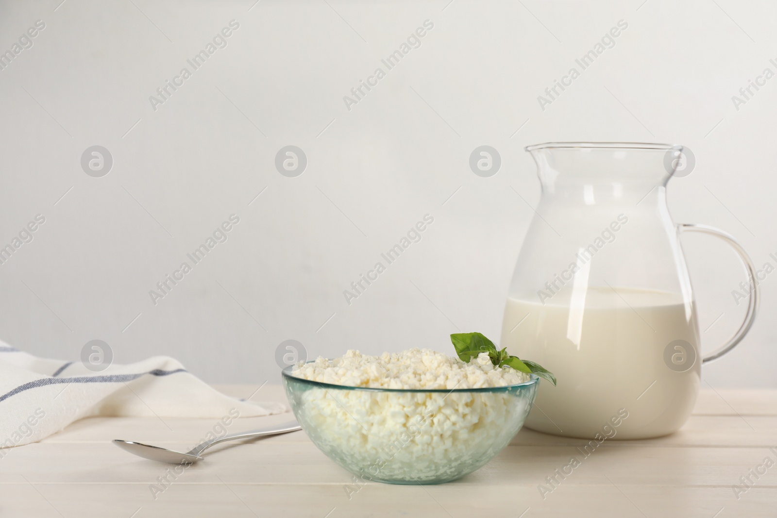 Photo of Delicious fresh cottage cheese with basil and milk on white wooden table. Space for text
