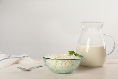 Delicious fresh cottage cheese with basil and milk on white wooden table. Space for text