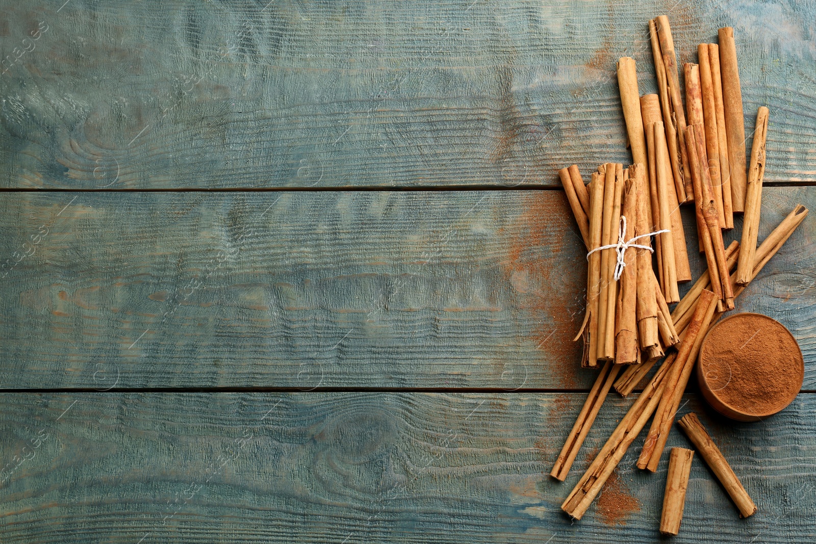 Photo of Aromatic cinnamon sticks and powder on light blue wooden table, flat lay. Space for text