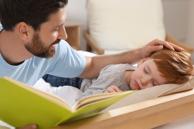 Photo of Father reading book with his child on bed at home, closeup