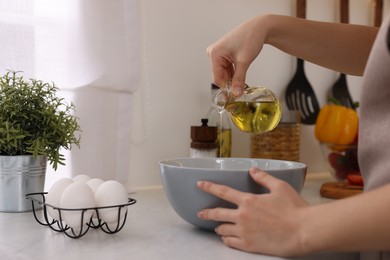 Cooking process. Woman pouring oil from bottle into bowl at light countertop indoors, closeup