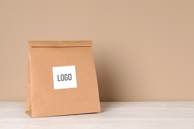 Image of Paper bag with logo on table against beige background. Space for text