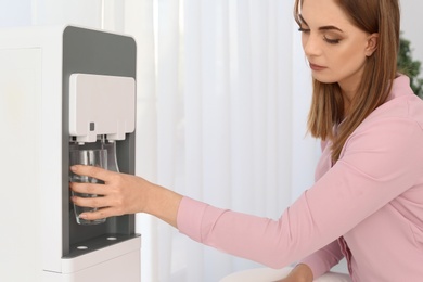 Photo of Woman filling glass from water cooler on light background