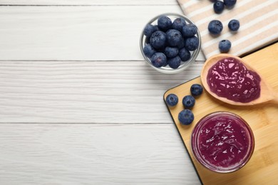 Photo of Delicious blueberry jam and fresh berries on white wooden table, flat lay. Space for text