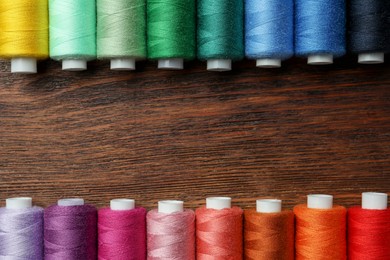Photo of Frame of colorful sewing threads on wooden table, flat lay. Space for text