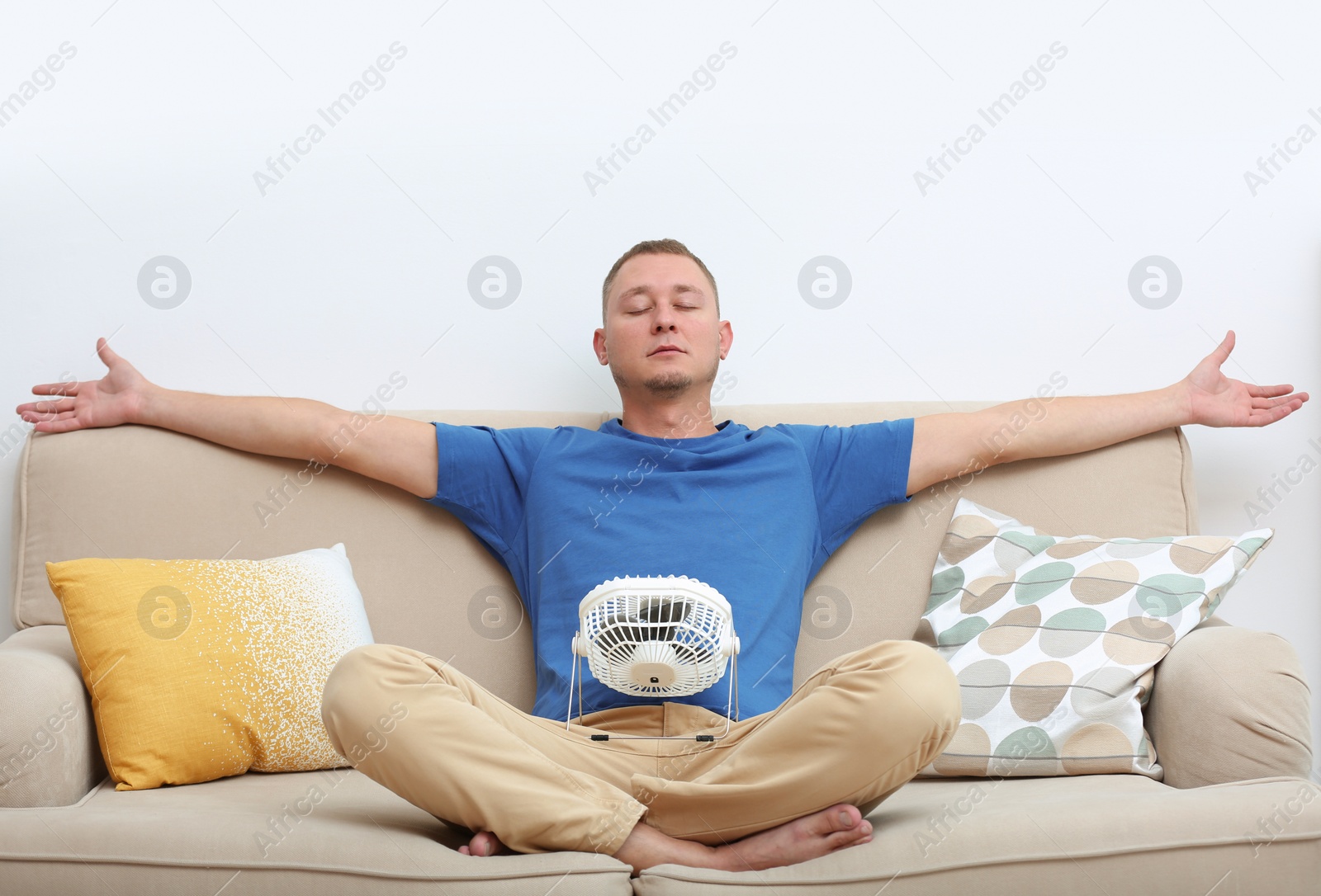 Photo of Young man refreshing in front of small fan at home. Summer heat