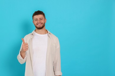 Photo of Young man showing thumb up on light blue background, space for text