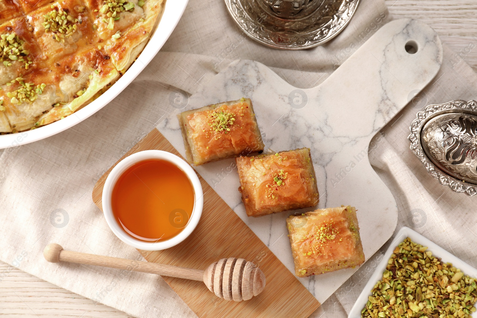 Photo of Delicious sweet baklava with pistachios and honey on table, flat lay