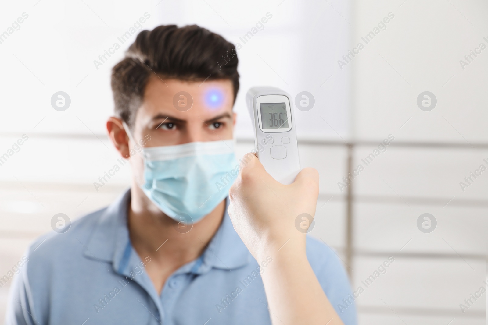 Image of Doctor measuring man's temperature indoors, closeup. Prevent spreading of Covid-19