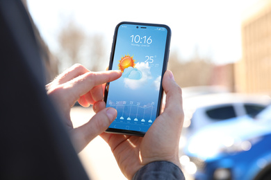 Man using weather forecast app on smartphone outdoors, closeup