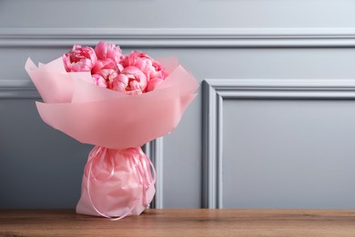 Photo of Bouquet of beautiful pink peonies on wooden table near grey wall. Space for text