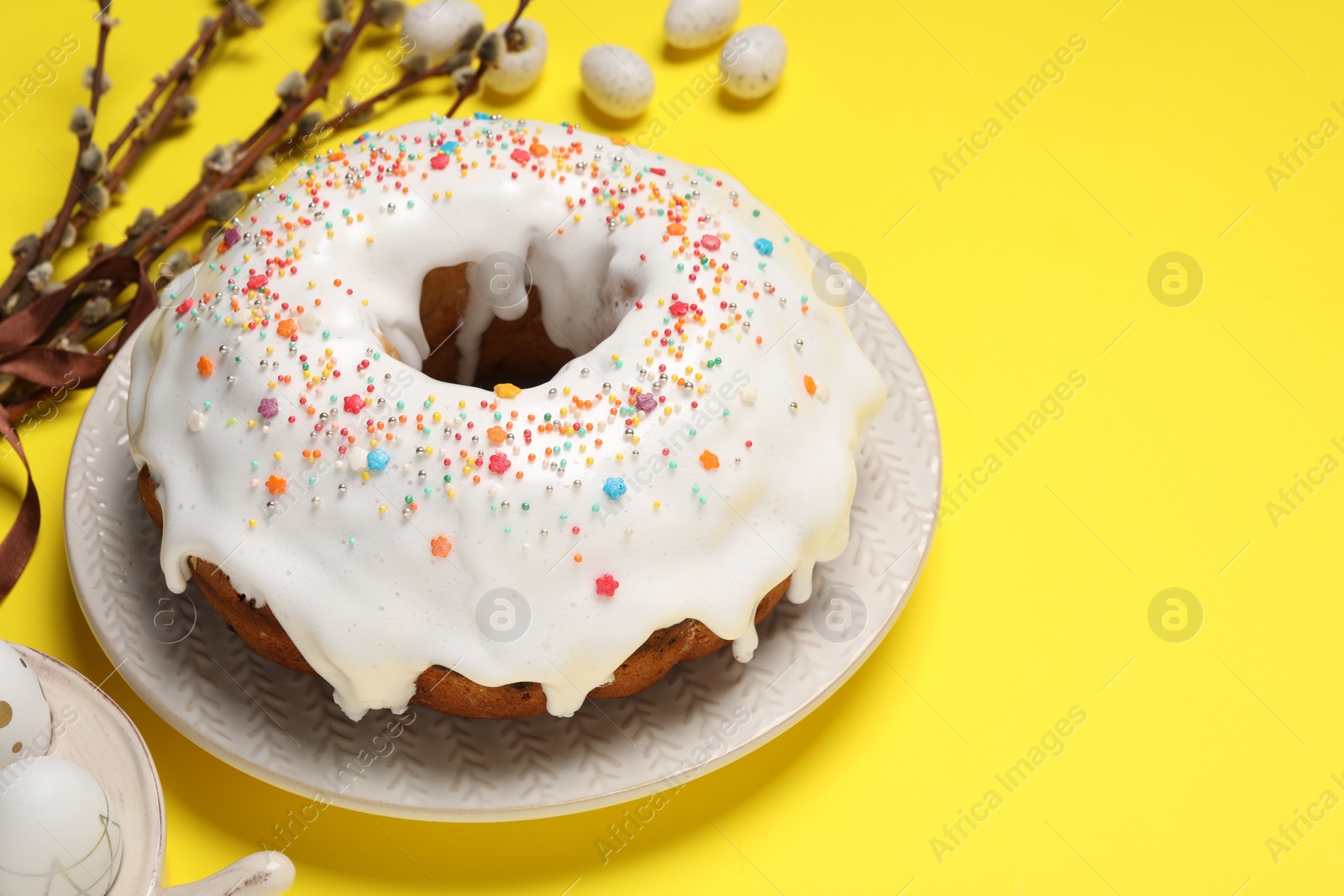 Photo of Easter cake with sprinkles, painted eggs and willow branches on yellow background, space for text