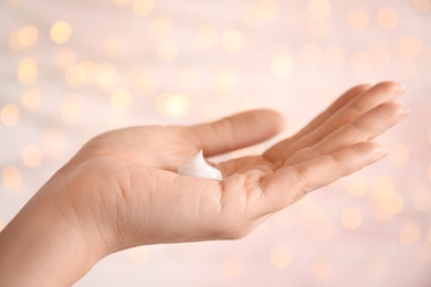 Woman applying hand cream on blurred background, closeup